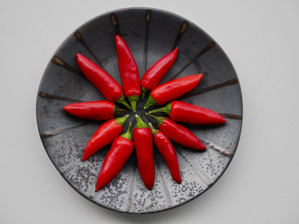 Aerial view of red hot chilis on black ceramic plate. - Фото, изображение