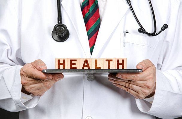 Un medico maschio in possesso di una tavoletta e blocchi di legno in rilievo con lettere alfabeto ortografia salute. Concetto di sanità e medicina. - Foto, immagini
