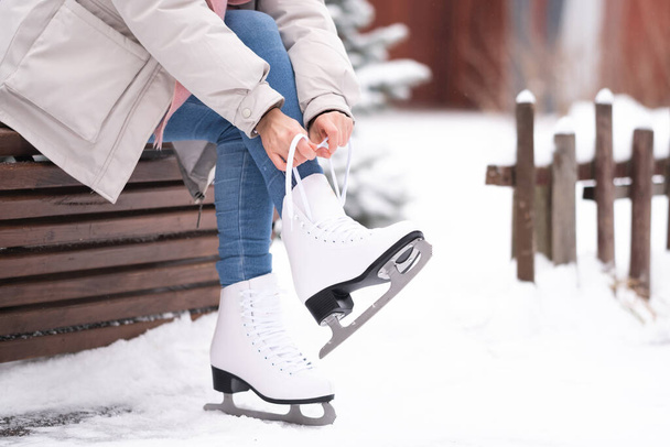 A girl laces up her skates while sitting on a park bench. A young woman came to skate at the rink. - Photo, Image