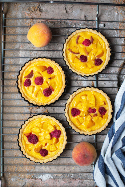 Baked custard tartlets with raspberries and peaches. Close up. - Фото, изображение