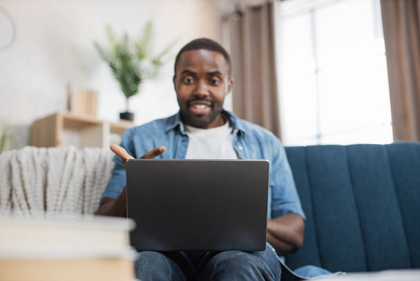 Happy african man sitting on couch and using laptop - Foto, imagen