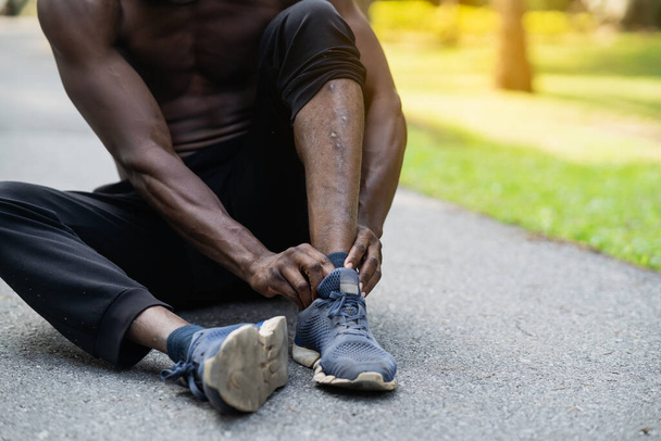 Afrykański biegacz siedzi na torze joggingowym i czuje ból w kostce, kopiuje przestrzeń. Koncepcja urazu sportowego - Zdjęcie, obraz