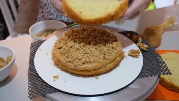 Selective focus. Confectioner placing a layer of cake over the dulce de leche and walnut filling. - Footage, Video