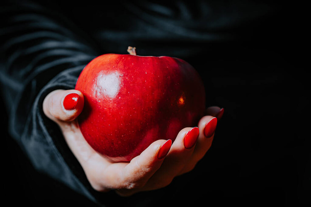 Witch woman in black offers red apple as symbol of temptation, poison. Fairy tale, white snow wizard concept. Spooky halloween, cosplay.  - Foto, Imagem