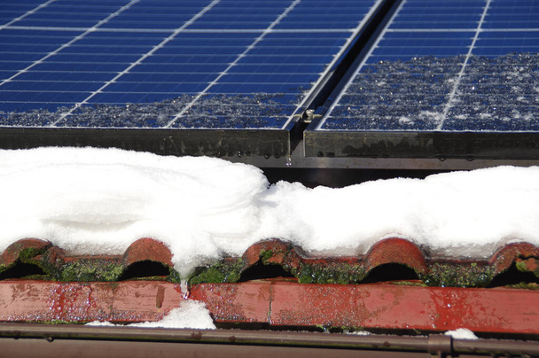 Pannelli solari coperti di neve. Impianto fotovoltaico elettrico sul tetto della casa durante la stagione invernale in una giornata di sole. Produzione domestica di energia alternativa in caso di freddo. - Foto, immagini