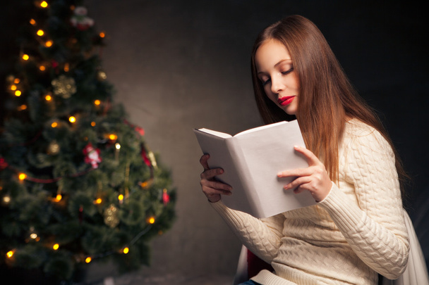 Mulher na frente da árvore de Natal livro de leitura
 - Foto, Imagem