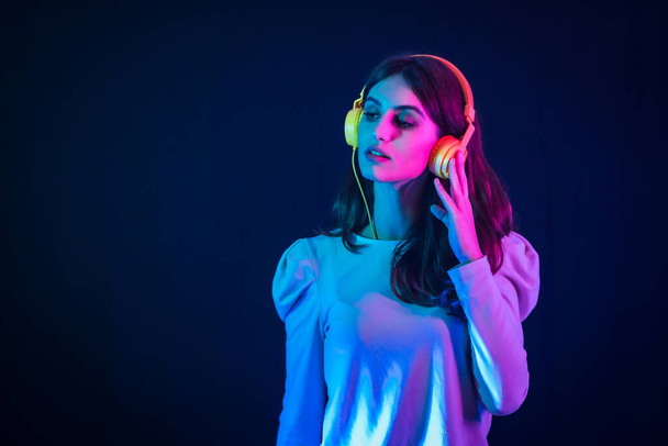 Young caucasian brunette with yellow headphones on a black background, illuminated in a disco with neon lights - Zdjęcie, obraz