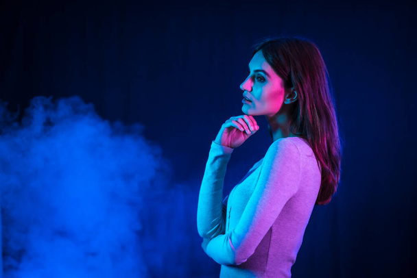 Portrait of a young brunette Caucasian woman in a white t-shirt dancing a disco with a black background. Neon lights with a background smoke - Fotografie, Obrázek
