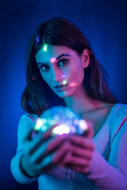 A young brunette Caucasian woman in a white t-shirt on a black background. Neon lights, illuminated with a disco light in hand, vertical photo - Zdjęcie, obraz