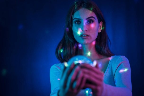A young brunette Caucasian woman in a white t-shirt on a black background. Neon lights, illuminated with a disco light in hand, sweet look - Zdjęcie, obraz