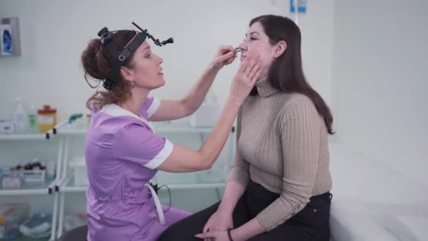 Otolaryngologický koncept. Pozitivní žena otorhinolaryngolog kontrolu nosu s otoskopem svého pacienta v nemocnici. Nosní kongesce, sinusitida, koncepce alergie. Pacientka na moderní ORL klinice - Záběry, video