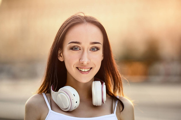 Happy young woman with cordless headphones on neck outside. - Valokuva, kuva