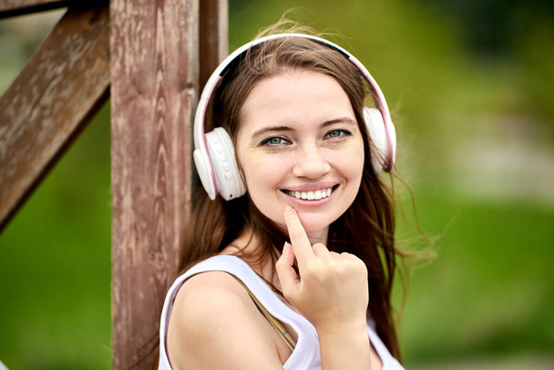 Young woman in cordless headphones is smiling outdoors. - Фото, зображення