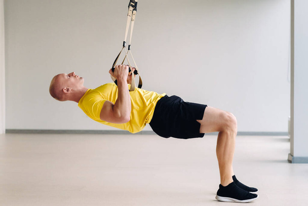 A focused male athlete performing an exercise on functional loops in the gym. - Photo, Image