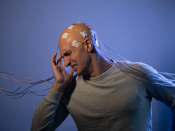 Un joven con la cabeza enredada en cables, gritando aferrándose a la cabeza, - Foto, imagen