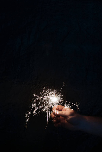 Hand with sparkler on dark background. Celebrating new year with sparkler. Hand holding sparkler on dark background. Christmas fun. New year concept. - Fotografie, Obrázek