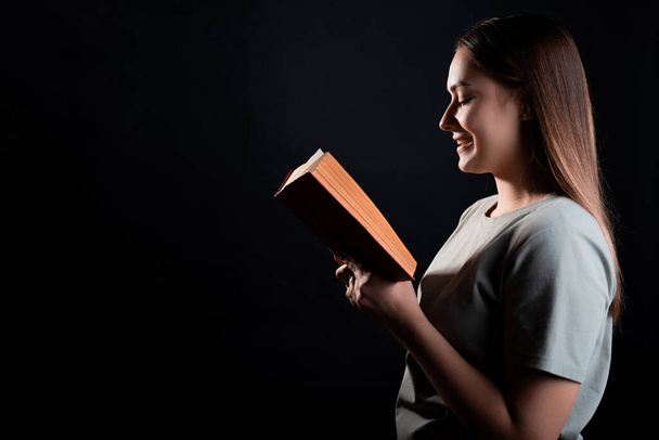 Een boek lezen, studeren of genieten van een roman. Jong brunette in een T-shirt met een open boek - Foto, afbeelding