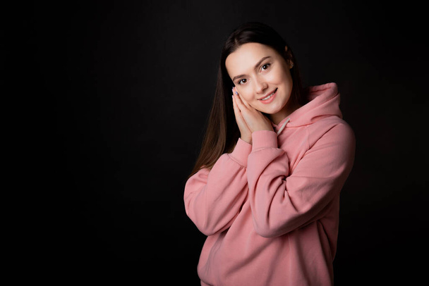 Cute young brunette in a pink hoodie, portrait on a black . - Photo, Image