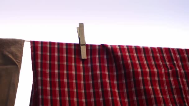 Красная рубашка висит на стиральной линии и высыхает после того, как прачечная снята крупным планом - Кадры, видео