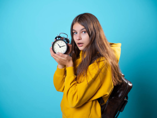 Hurry up, concept. A young brunette in a youth hoodie holds an alarm clock - Фото, изображение