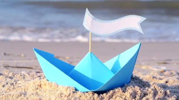 Niebieski papierowy jacht na piaszczystej plaży nad morzem w słoneczny letni dzień. - Materiał filmowy, wideo