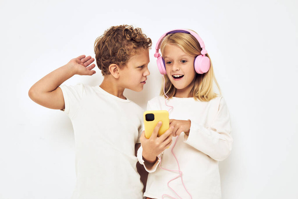 Two preschool children boy and girl smiling with phone in hand fashion light background - Фото, зображення