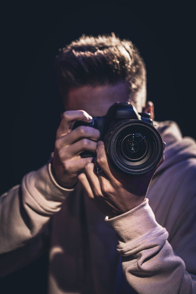Een man fotograaf met een camera neemt een foto in het donker. - Foto, afbeelding
