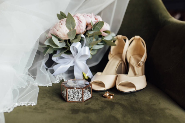 Wedding bouquet of white peonies, shoes and wedding rings on a wooden background - Foto, afbeelding