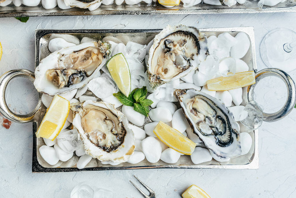 Verse oesters in een wit bord met ijs en citroen. Oesterdiner met champagne in restaurant. bovenaanzicht. - Foto, afbeelding