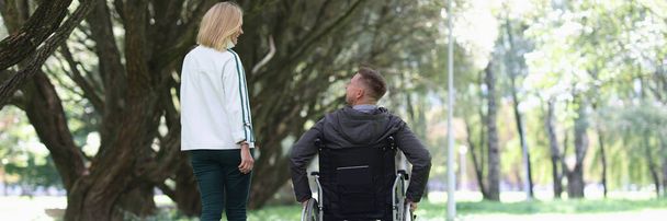 Man in wheelchair is walking in park with his girlfriend - Фото, изображение