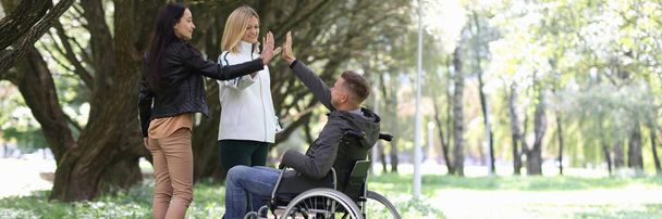 Άνδρας με ειδικές ανάγκες σε αναπηρική καρέκλα δίνει πέντε σε γυναίκες φίλους στο πάρκο - Φωτογραφία, εικόνα