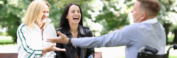 Mozgáskorlátozott férfi tolószékben kommunikál és nevet a nőkkel a parkban - Fotó, kép
