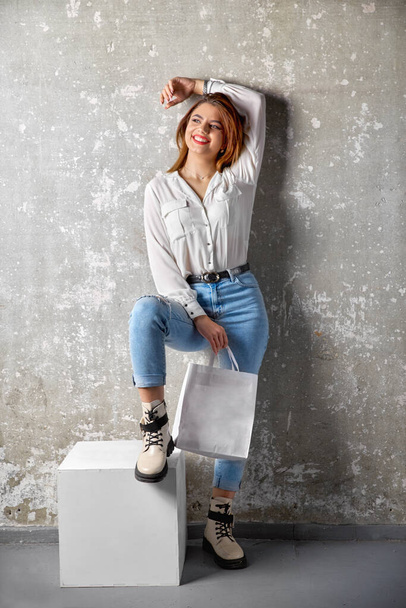 Close-up of hipster girl wearing blue jeans and holding blank craft paper package, mock-up of template white package with handles. Template can be used for you design - Foto, Imagen