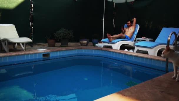 リラックスした男はプールの日光浴の近くの別荘で時間を費やしていると誰かと話をする - 映像、動画