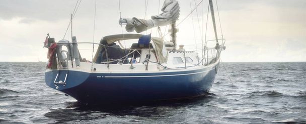 Sloop azul equipado iate ancorado ao largo da costa da Inglaterra sob o céu escuro depois de uma tempestade. Navegando em mau tempo. Uma paisagem marinha dramática. Raios solares através das nuvens - Foto, Imagem