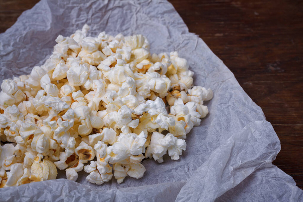 Heap of ready salted buttered popcorn on white paper brown wooden table background, close up shot - Foto, immagini