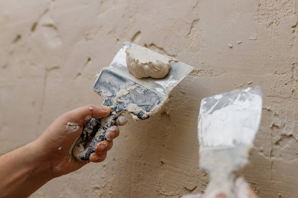 Αρσενικά χέρια με σπάτουλα χρησιμοποιώντας στόκος για τοίχο, οικοδόμος κάνει γενική επισκευή. - Φωτογραφία, εικόνα
