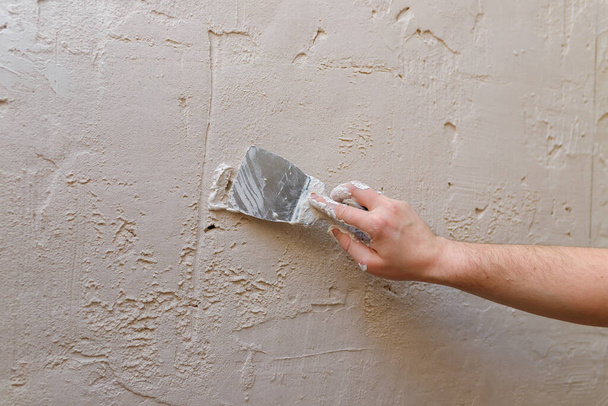 Manos masculinas con espátula usando masilla para pared, constructor haciendo revisión. - Foto, imagen