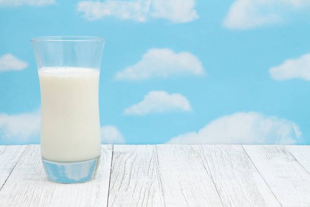 Studená sklenice mléka na ošlehaném dřevě s jasnou oblohou s kopírovacím prostorem pro vaši zprávu - Fotografie, Obrázek