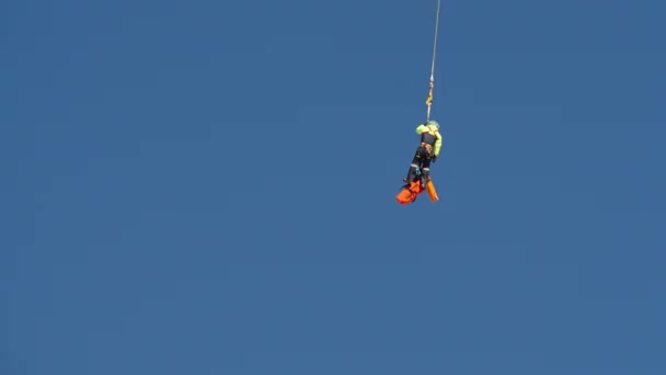 Redder vliegend op veiligheidstouw in de blauwe lucht, een reddingsmissie op grote hoogte - Video