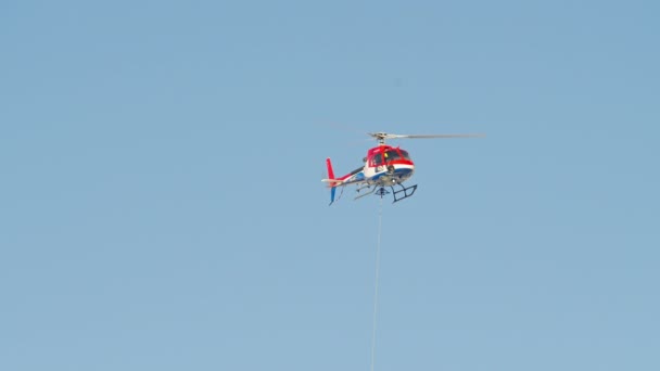 Pelastuspartio helikopteri turvaköysi lentää korkealla sinisellä taivaalla auringonpaisteessa - Materiaali, video