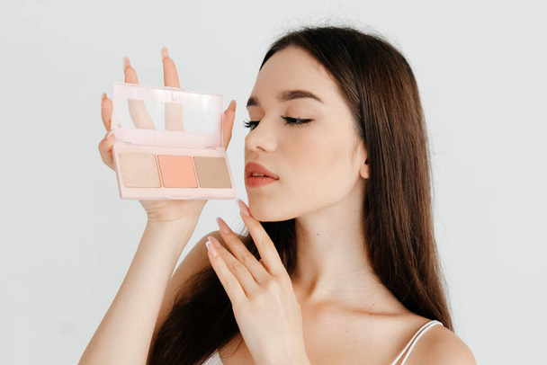 Κοντινό πλάνο φωτογραφία του ελκυστικό κορίτσι κρατώντας μια παλέτα contouring, θέλει να κάνει το τέλειο make-up, πάνω από το λευκό φόντο χρώμα - Φωτογραφία, εικόνα