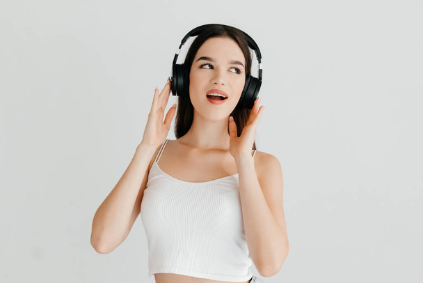 Young woman wearing casual clothes - white top and jeans, black headphones, listening to music - Foto, immagini