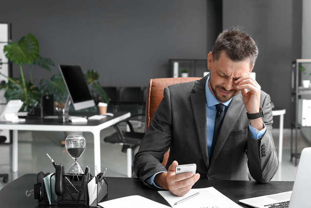 Stressed businessman with mobile phone sitting at table in office - Foto, Imagen