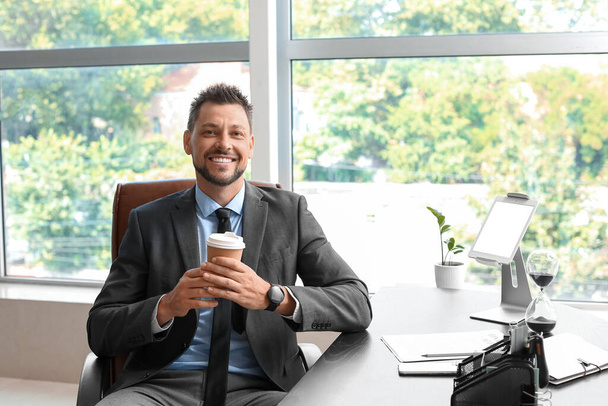 Hombre de negocios guapo con taza de café sentado en la mesa en la oficina - Foto, imagen