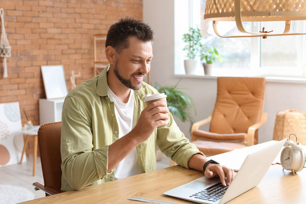 Красивий чоловік з чашкою кави працює за столом в офісі
 - Фото, зображення
