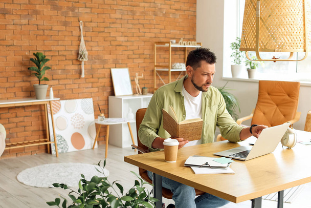 Knappe man werkt met notebook en laptop aan tafel in het kantoor - Foto, afbeelding