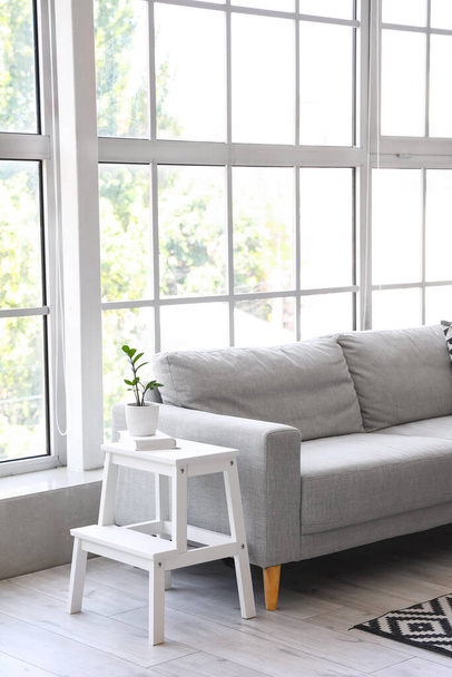 Taburete paso blanco con maceta y libro cerca de sofá en sala de estar - Foto, imagen