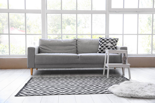 Сірий диван і білий стілець біля вікна
 - Фото, зображення
