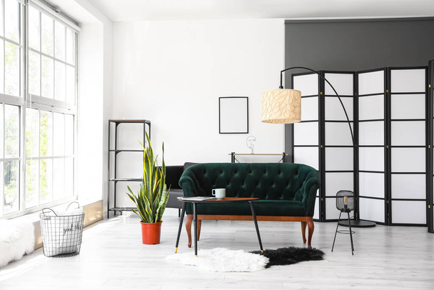 Інтер'єр світлої вітальні з зеленим диваном, столом і лампами
 - Фото, зображення